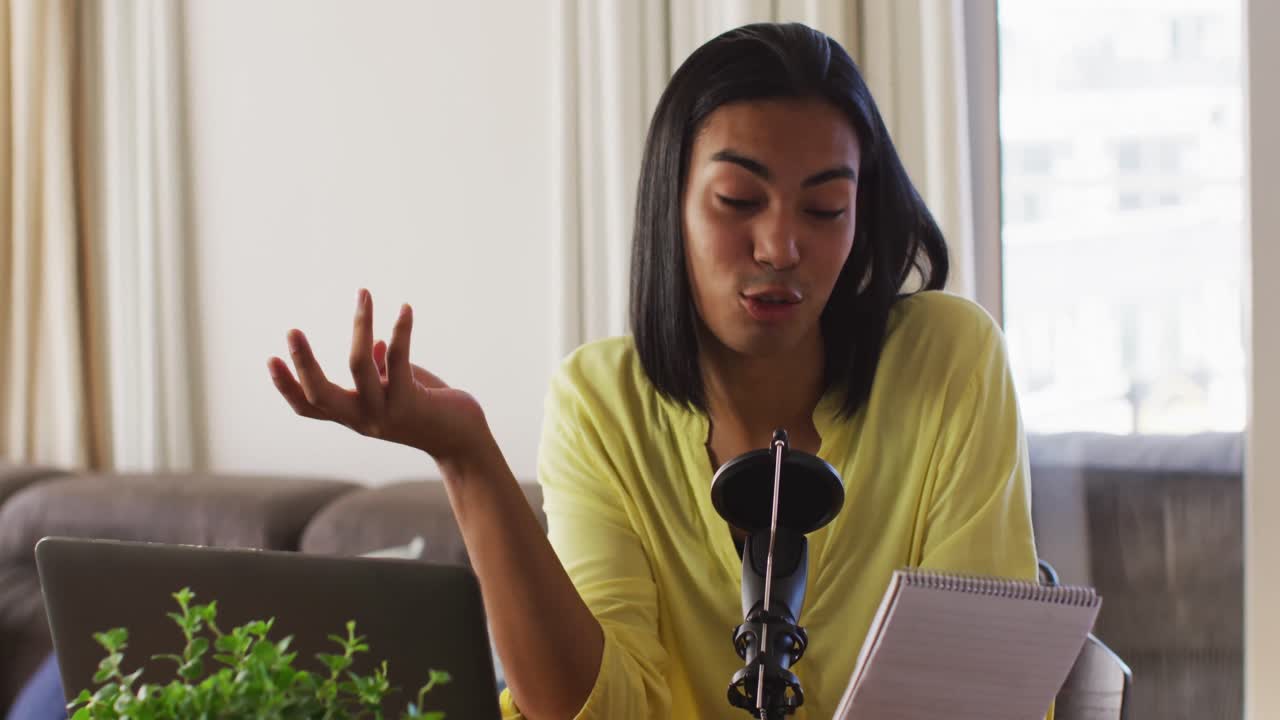 Persona gender fluid multietnica che registra un podcast usando il laptop e leggendo appunti a casa.