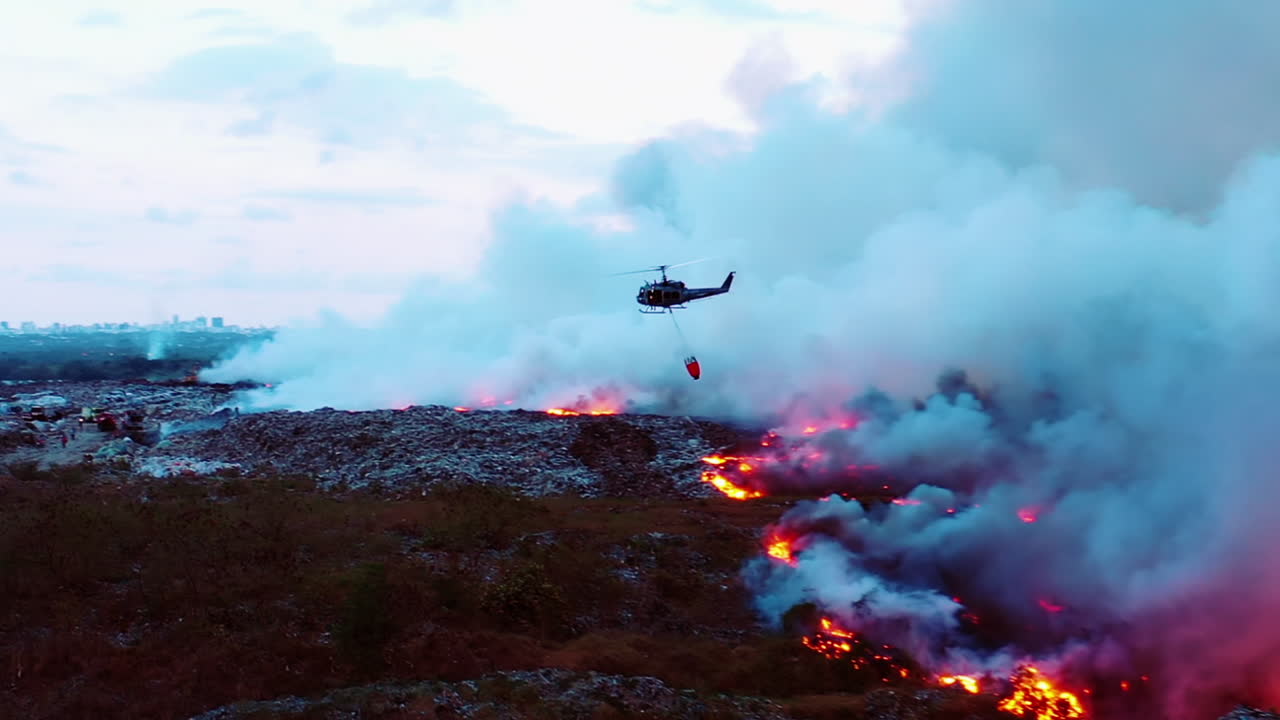 Lanzamiento de agua desde helicóptero sobre incendios forestales en California, toma aérea de dron siguiendo a un helicóptero combatiendo un incendio, rodeado de humo denso, atardecer sombrío en Los Ángeles, EE. UU.