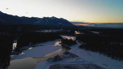 Toma-Aérea-Del-Hermoso-Paisaje-Invernal-Durante-La-Hora-Dorada,-Que-Muestra-El-Río-Con-Reflejo-Y-Majestuosas-Montañas-En-La-Distancia-En-Columbia-Británica,-Canadá