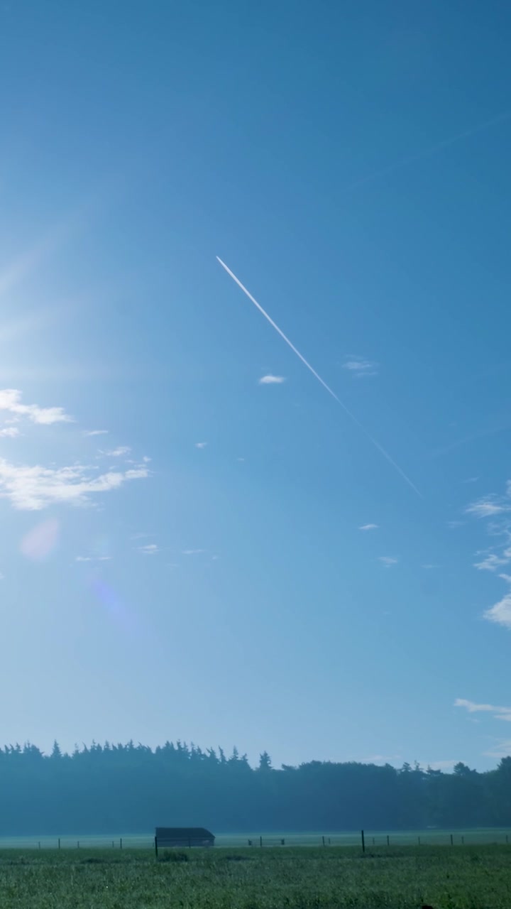 Scia di un aereo attraverso un cielo azzurro limpido sopra un paesaggio rurale