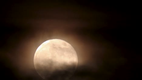 primer plano nocturno de la luna llena saliendo, mientras está envuelto por nubes ominosas