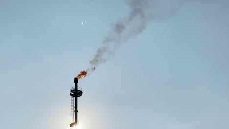 Telephoto-of-Gas-Flare-flame-burning-releasing-smokestack,-sunset,-handheld