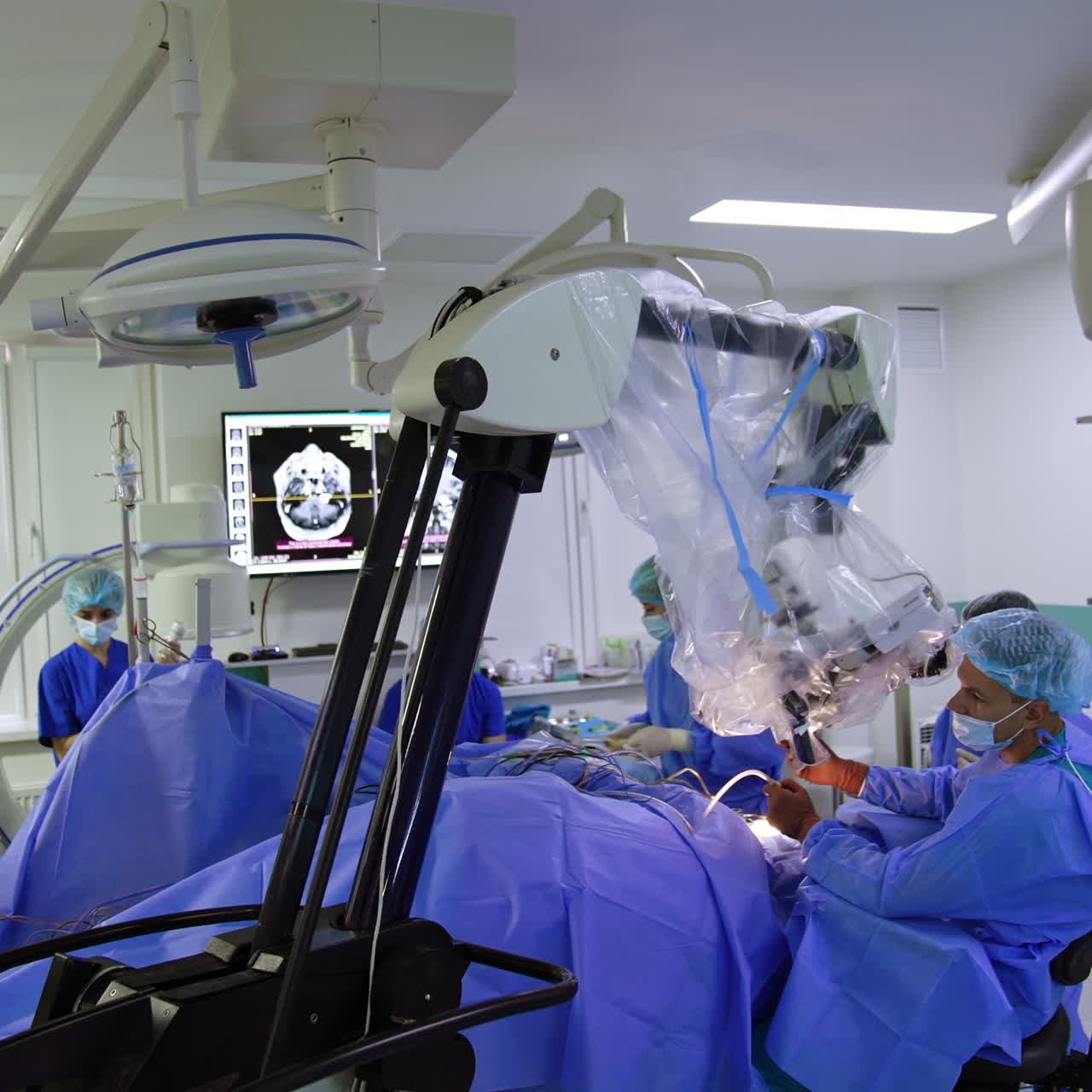Modern technological microscope stands in the surgery room above the patient. Neurosurgeon sitting at operational table looks at binoculars applying tools.