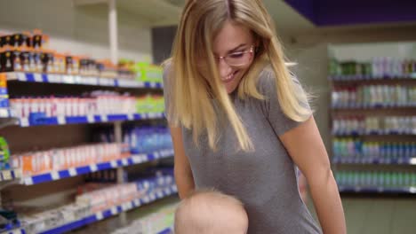 pequeño bebé y su madre se divierten en el supermercado. niño lindo está sentado en un carrito de comestibles, mientras que su madre está empujando el