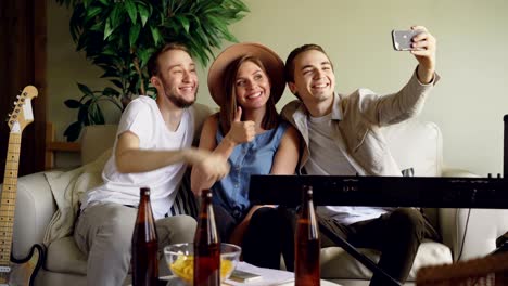 playful young people from musical band are taking selfie with smartphone, posing and making funny faces, laughing and hugging. musical instruments are visible.