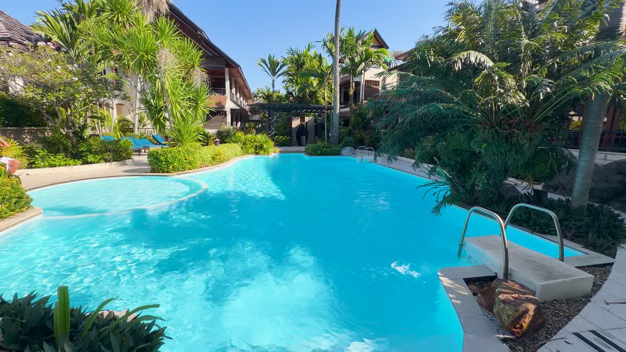 Statisk vidvinkelbillede af en funklende turkis swimmingpool omgivet af resortets frodige tropiske beplantning