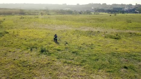 person riding a green motorcycle in a dirt field area enduro  off road riding with a drone following from above and behind.