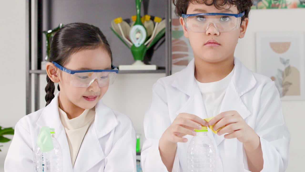 Dua siswa muda Asia mengenakan kacamata pengaman saat melakukan eksperimen sains di ruang kelas