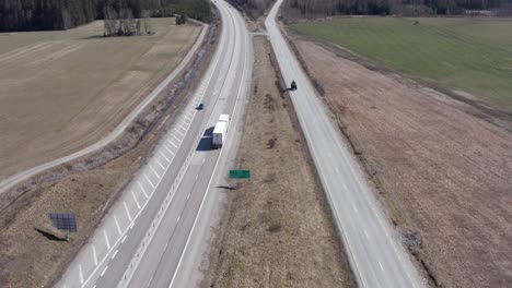 drone shot rising over highway next to country road in sweden with car, truck and tractor driving