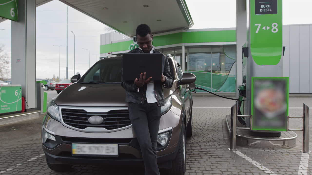 Un lavoratore freelance afroamericano tiene un portatile in mano e si appoggia a un'auto di lusso mentre lavora