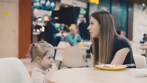 young beautiful mother giving daughter drink juice through straw sitting in cafe