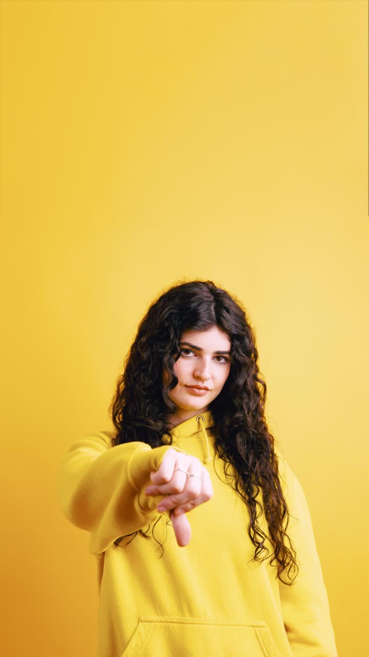 Woman gives thumbs down in yellow hoodie