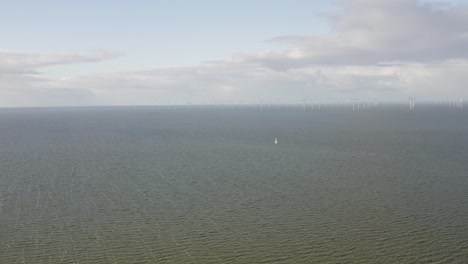 Toma-Aérea-De-Un-Velero-Acercándose-A-Un-Gran-Parque-Eólico-En-El-Mar-En-Los-Países-Bajos-En-Un-Hermoso-Día-Soleado