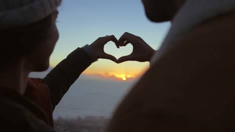 couple in love looking at sunset with finger heart