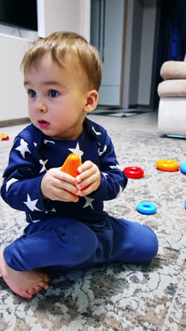 nice baby boy sits on the floor holding a toy in his hands. kid plays with his toys in the living room. vertical video
