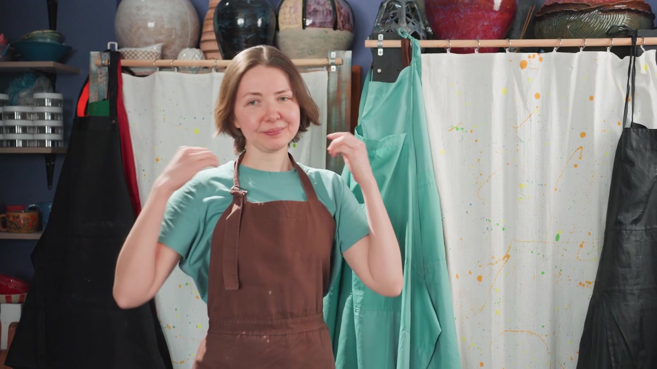 Una donna sceglie con cura un grembiule pratico tra la varietà disponibile sugli scaffali espositivi di un laboratorio di ceramica