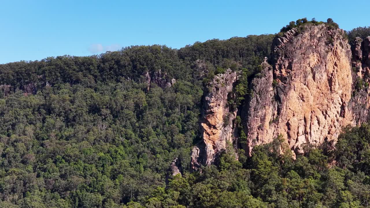 Drone footage captures the majestic rhyolite volcanic plugs of Nimbin Rocks surrounded by lush eucalyptus forests under clear blue skies