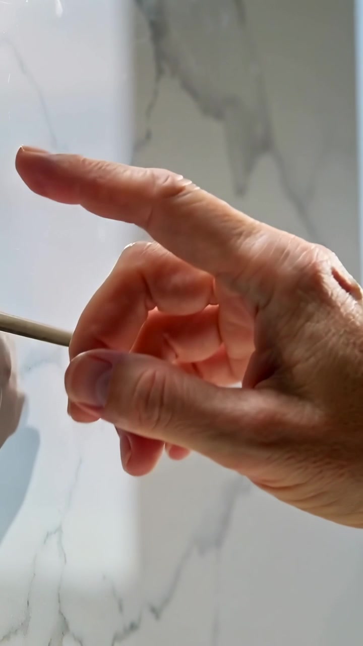 Vertical video: Approaching right hand touching round white cap on marble wall, prying with stylus