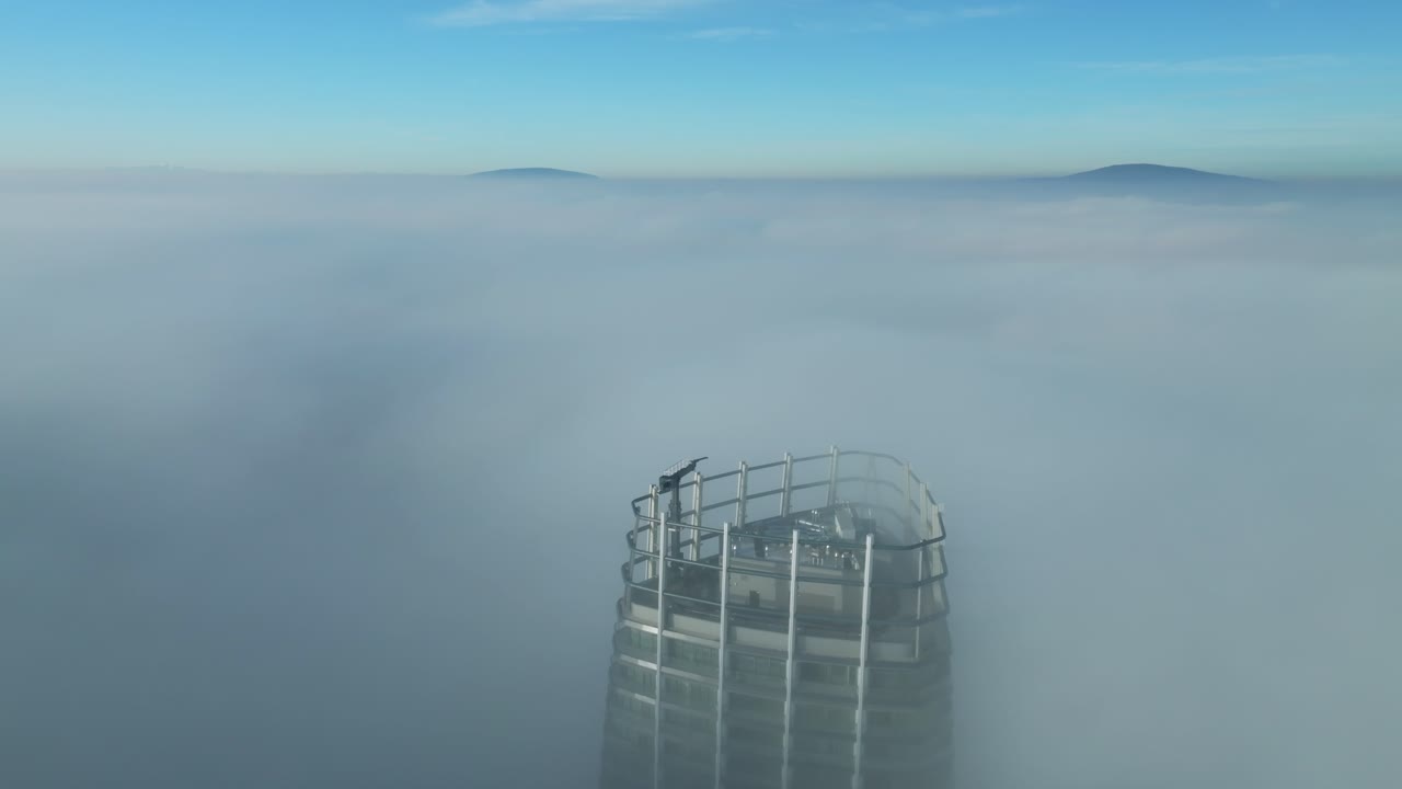 공중 영상: 드론이 기울어져서, 은 해가 뜨는 구름을 고 나가는 외로운 마천루를 보여줍니다.
