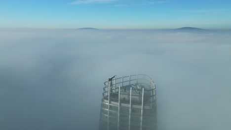 aerial footage: drone tilts up, revealing lone skyscraper breaking through thick sunrise clouds