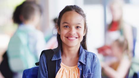 Retrato-De-Una-Feliz-Colegiala-Birracial-Con-Diversos-Escolares-En-Segundo-Plano-En-La-Escuela