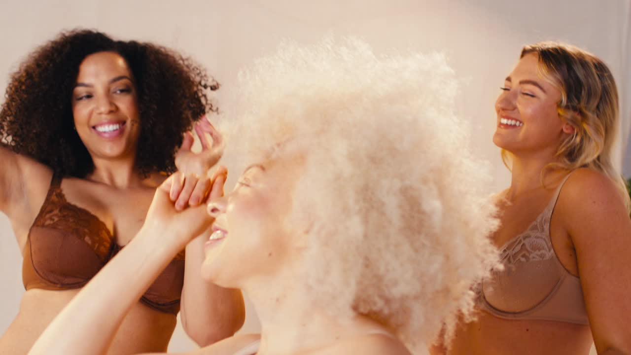 다양한 여성 친구 그룹이 속옷을 입고 몸의 긍정성을 홍보하고 스튜디오에서 춤을 추고 있습니다.