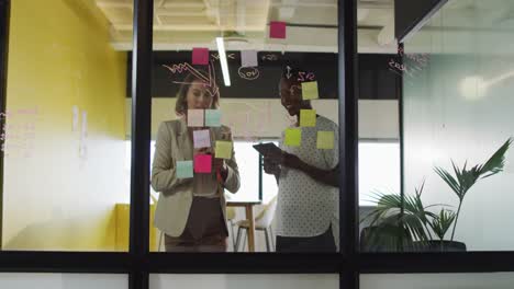 Two-diverse-female-colleagues-making-notes-and-discussing-at-work