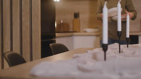 camera focuses on woman placing dishes on the table decorated with candles and a tablecloth for christmas dinner