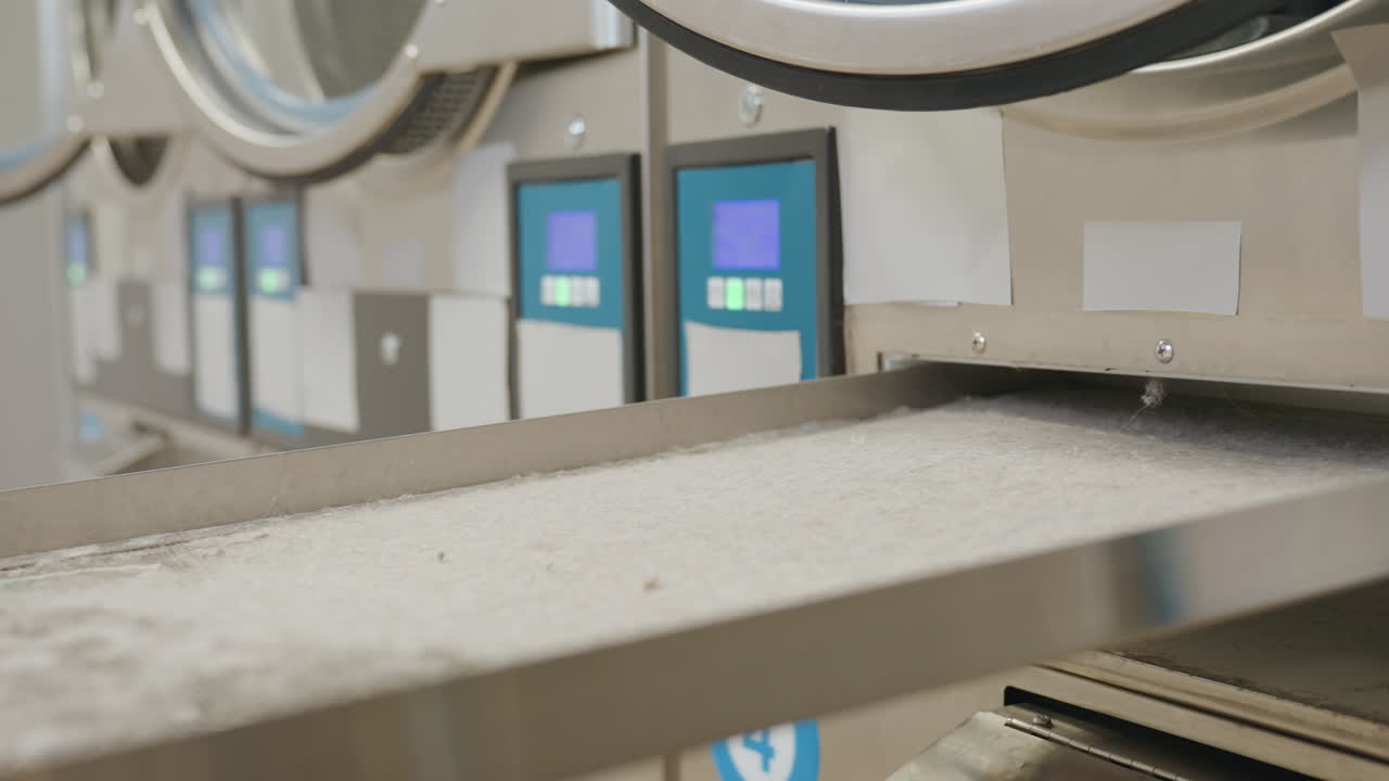 Industrial washing machine drawer being pushed back inside as worker hand locks it with key, showing process of maintenance and secure operation in modern laundromat interior