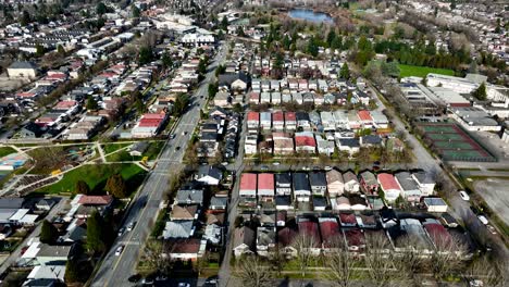 Cars-Driving-Through-Victoria-Drive-With-Trout-Lake-In-The-Distance-In-Vancouver,-British-Columbia,-Canada