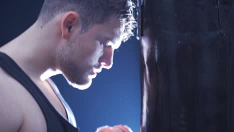 portrait of male boxer beating punching bag in dark gym.