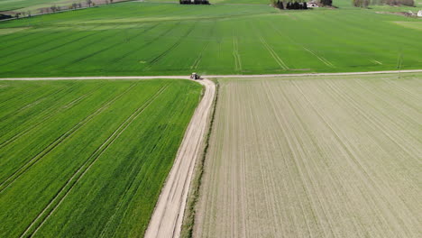 Establishing-aerial-view-of-farmland-landscape-and-tractor-driving-dusty-road