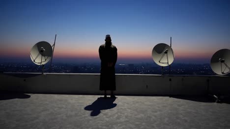 imam stands on a rooftop at dawn, overlooking a city skyline with satellite dishes in the foreground, creating a serene and contemplative scene