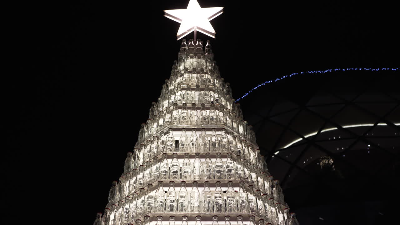 Original christmas tree made of recycled glass bottles is illuminated by a bright star