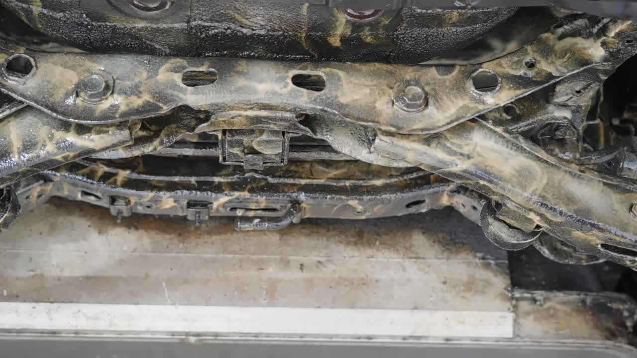 Close up low angle sliding view of electric vehicle underside after lanolin rust protection treatment