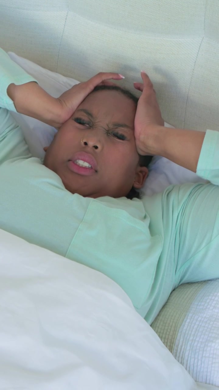 Vertical video: Opening eyes, woman in mint top pressing temples, reacting to headache in bed