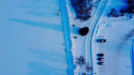 Sobrevuelo-Aéreo-De-Invierno-De-4k,-Reflejo-De-La-Puesta-De-Sol,-árboles-De-Sombra,-Parque-Cubierto-De-Nieve,-Camino-De-Patinaje-Conectado-A-La-Pista-De-Hielo-Artificial-Más-Grande-De-Canadá-Con-Parejas-Adultas-Patinando-Junto-Al-Estacionamiento-Edm-Victoria-Park3-6