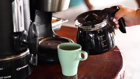 hand pouring coffee into a green mug