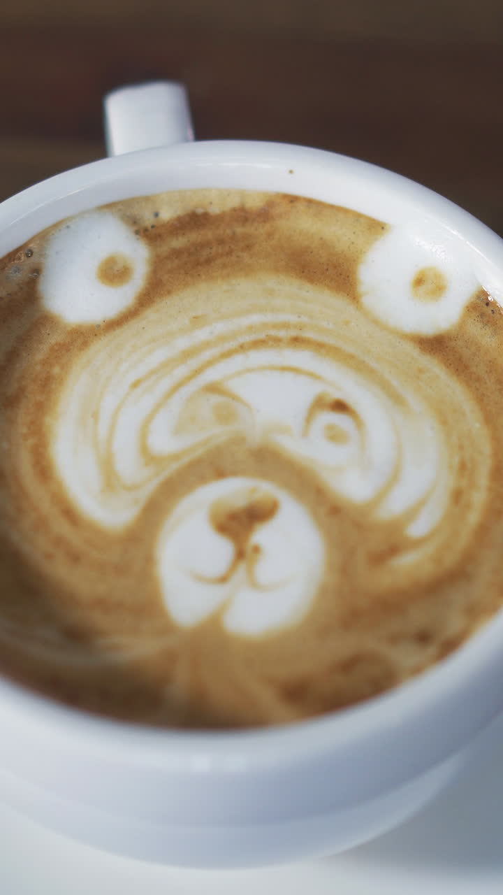 Turning a cup of coffee with latte art to show the drawing in the form of a bear. Cappuccino, latte art. Vertical video.