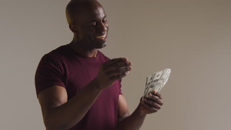 studio shot of excited mature man celebrating winning cash prize kissing and throwing handful of 100 dollar bills in the air