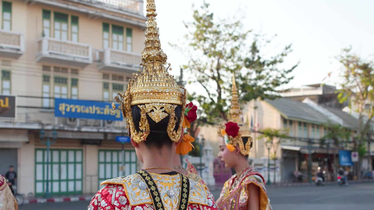 Danzatrici classiche thailandesi con elaborati copricapi dorati si esibiscono all'aperto sullo sfondo di una storica strada di Bangkok