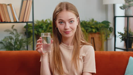 thirsty young woman sitting at home holding glass of natural aqua make sips drinking still water