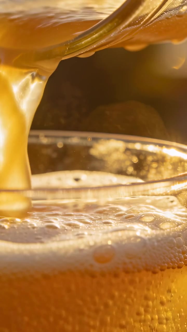 Video verticale: Versamento da beccuccio, birra dorata che riempie un bicchiere trasparente su un bancone, formando schiuma.