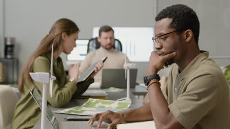 side view of man working using laptop and writting notes sitting at desk in the office