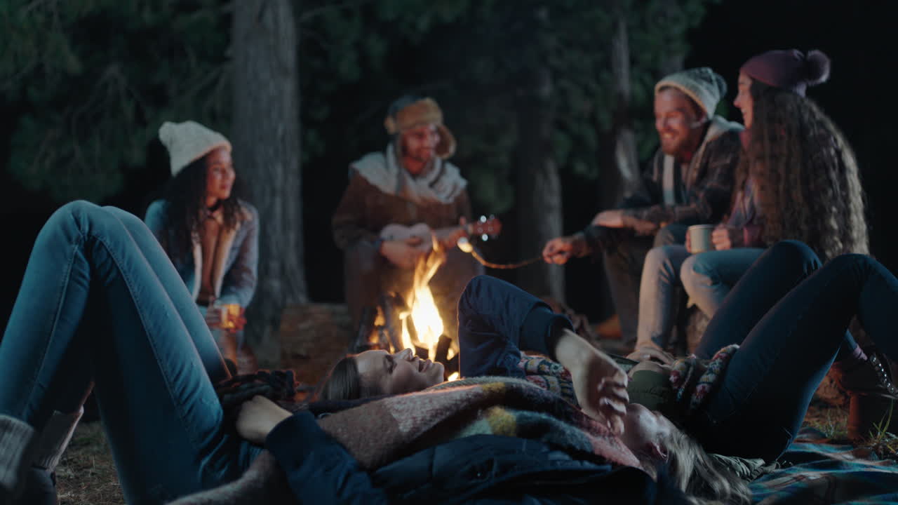 캠핑 친구들은 별을 바라보며 밤하늘을 가리키며 별들을 바라보며 담소를 나누고 캠프파이어 옆에 앉아 함께 저녁을 즐기고 있습니다