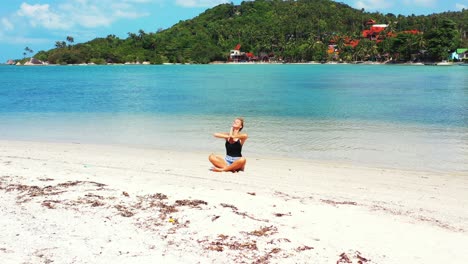 happy woman with a big smile practicing yoga and meditating on the sandbar in thailand