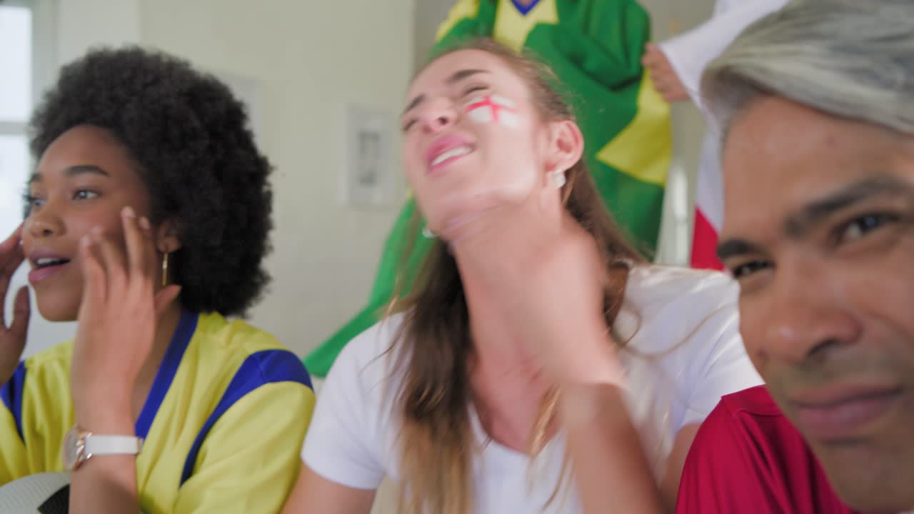 Tifosi diversi sul divano che guardano una partita in TV, una donna di mezza età con il viso dipinto con la bandiera dell'Inghilterra sorride e poi sospira