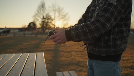 Person-holding-drone-remote-and-guiding-the-drone-back-to-land-on-a-picnic-table