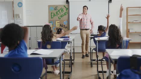 escolares diversos en los escritorios levantando las manos y el maestro masculino en el aula de la escuela primaria