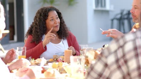 happy diverse male and female friends eating thanksgiving celebration meal in sunny garden